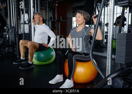 Un uomo e una donna sono seduti su palline colorate in palestra Foto Stock