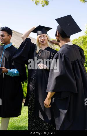 Diversi laureati in cappelli e abiti festeggiano in giardino, sorridono e chiacchierano insieme Foto Stock