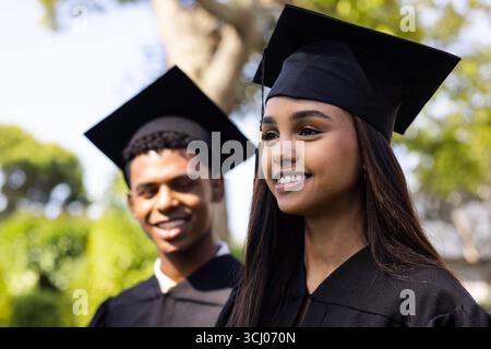 Giorno della laurea, diversi studenti in berretti e abiti sorridenti in giardino Foto Stock