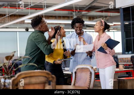Team che collabora con entusiasmo in un ufficio moderno, condividendo idee e documenti Foto Stock