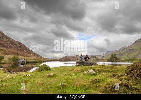 Galles del Nord, Regno Unito. Settembre 2025. Meteo nel Regno Unito: Nuvole piovose oscurano il cielo nel Galles del Nord. Due persone sono sedute insieme su una roccia di fronte ai laghi di Cregennan (Llynau Cregennan) ammirando il pittoresco paesaggio. Crediti: Lee Hudson/Alamy Foto Stock