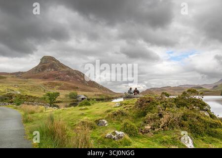 Galles del Nord, Regno Unito. Settembre 2025. Meteo nel Regno Unito: Nuvole piovose oscurano il cielo nel Galles del Nord. Due persone sono sedute insieme su una roccia di fronte ai laghi di Cregennan (Llynau Cregennan) ammirando il pittoresco paesaggio. Crediti: Lee Hudson/Alamy Foto Stock