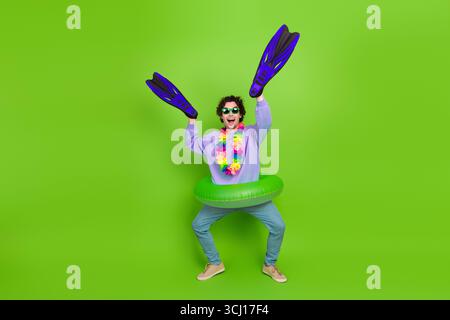 Uomo divertente che indossa abiti casual con pinne da bagno, anello gonfiabile e lei fiore su sfondo verde Foto Stock