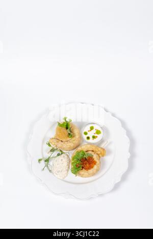 Elegante servizio di pancake gourmet con caviale rosso, lattuga fresca, salsa panna ed erbe aromatiche su un piatto bianco per il menu del ristorante. Foto Stock