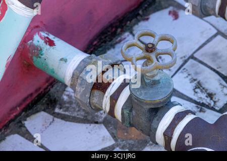 Ripresa ravvicinata di una valvola rotonda di arresto dell'acqua in metallo, molto arrugginita e invecchiata, su un serbatoio dell'acqua del tetto. Un'immagine dettagliata della texture che mostra la corrosione. Foto Stock