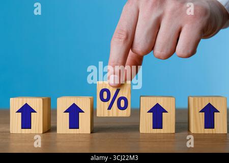 Uomo che mette un cubo di legno con il segno di percentuale tra gli altri con frecce su sfondo blu, primo piano Foto Stock