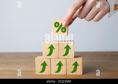 Donna che mette un cubo di legno con il segno di percentuale sopra gli altri con frecce su sfondo chiaro, primo piano Foto Stock
