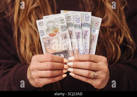 Mani femminili che tengono banconote in sterline britanniche. Donna che mostra contanti in valuta del Regno Unito. Settore finanziario e bancario. Ricchezza personale e risparmi. Foto Stock