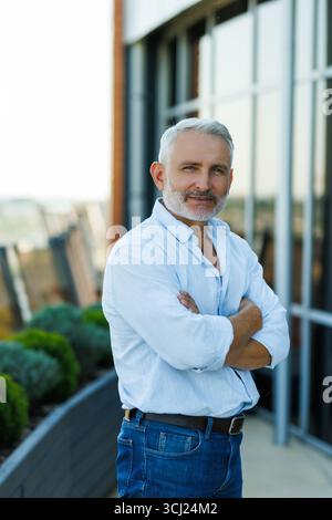 un uomo maturo sta meditando sulla terrazza del tetto della casa sullo sfondo del paesaggio urbano al tramonto. Copia spazio. Foto Stock