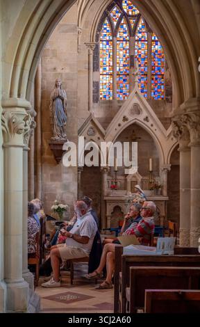 Langrune-Sur-Mer, Francia - 08 09 2025: Veduta dettagliata di una cappella e delle persone sedute sulle panchine della chiesa, dell'altare e delle vetrate colorate all'interno del sa Foto Stock