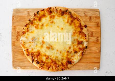 Una pizza al formaggio appena sfornata si trova senza fette su un tagliere rotondo di legno. Foto Stock