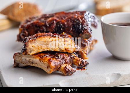 Costolette glassate per barbecue di maiale su un tagliere bianco. Foto Stock