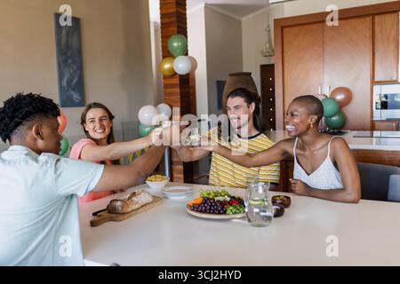 Gli amici brindano a casa, si divertono a festeggiare con cibo e risate. riunione, festa, cena, felicità, socializzazione Foto Stock