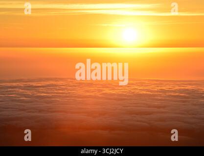 Un magnifico tramonto dorato visto dall'alto delle nuvole. Il sole brilla, emettendo una calda luce arancione e gialla su una soffice nuvola eterea Foto Stock