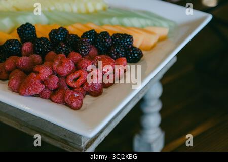 Una selezione di frutti vivaci, tra cui lamponi, more e meloni disposti ordinatamente su un piatto. Foto Stock