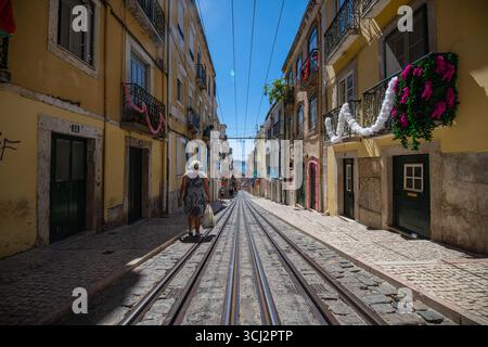 Una foto grandangolare e ad angolo basso di una strada ripida di Lisbona, che mostra le iconiche piste del tram, i classici ciottoli e un mix di architettura storica Foto Stock