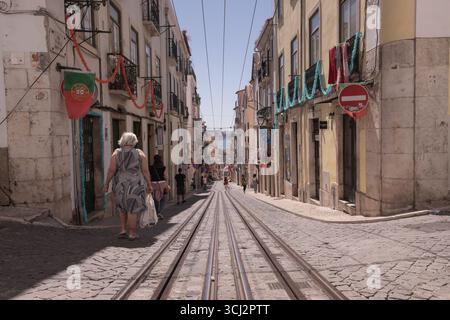 Una foto grandangolare e ad angolo basso di una strada ripida di Lisbona, che mostra le iconiche piste del tram, i classici ciottoli e un mix di architettura storica Foto Stock