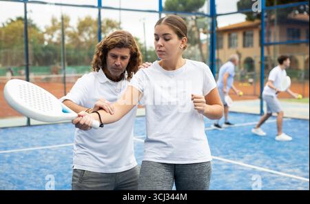 Ritratto di allenatore maschile concentrato che insegna giovane donna che gioca a padel Foto Stock