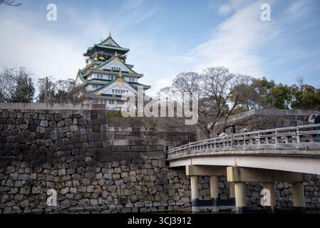 Castello di Osaka con Ponte di pietra e visitatori in Giappone. I turisti attraversano un ponte di legno verso il Castello di Osaka, incorniciato da fossati e mura di pietra. Foto Stock