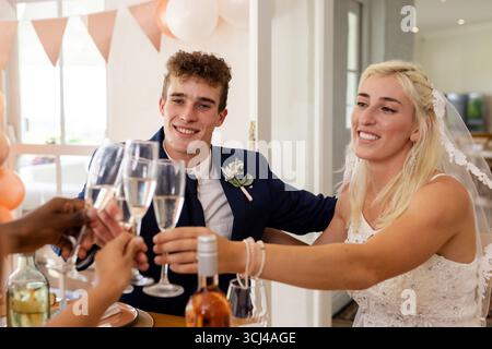 Sposa e sposo brindano con gli amici, celebrando un gioioso ricevimento di nozze all'interno Foto Stock