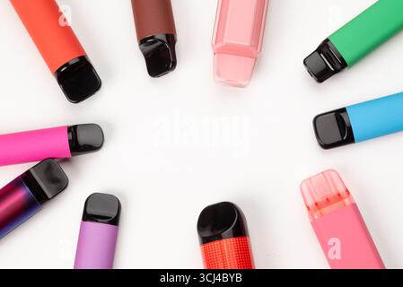 Varie penne monouso colorate disposte in cerchio su sfondo bianco, moderni dispositivi elettronici per fumatori. Foto Stock