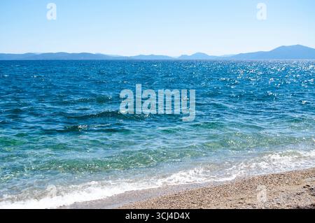Il mare con le montagne sullo sfondo. Onde di mare sulla spiaggia. Mare, cielo e spiaggia. Foto Stock