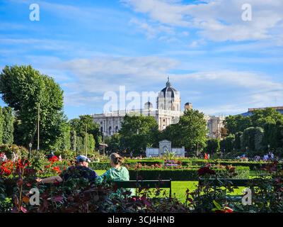 Visitatori che si rilassano al Giardino delle Rose di Volksgarten con il Museo Kunsthistorisches sullo sfondo - Vienna, Austria Foto Stock