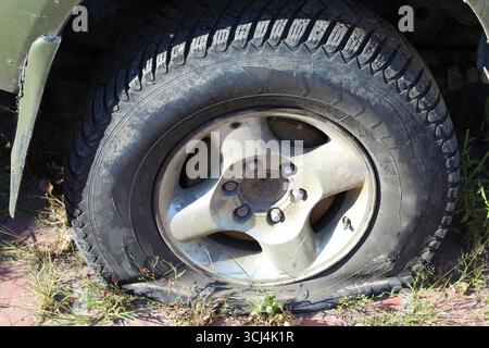Pneumatico sgonfio su una ruota danneggiata primo piano su fondo stradale esterno concetto di guasto incidente e necessità di riparazione Foto Stock