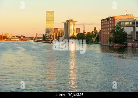 Berlino, Germania - 18 agosto 2025: Vista panoramica del fiume Sprea che riflette le sfumature dorate del tramonto con edifici moderni a Berlino, Germania. Foto Stock