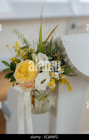 Elegante composizione floreale con rose, margherite e vegetazione collocate in un vaso di vetro, elegantemente attaccato a una scala bianca, perfetta per Foto Stock