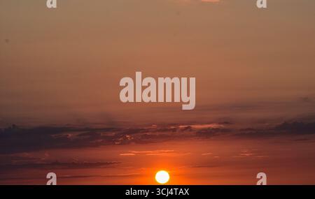 Tramonto con sole incandescente all'orizzonte, cielo magico e colorato pieno di toni caldi, creando un'atmosfera tranquilla e da sogno. Foto Stock