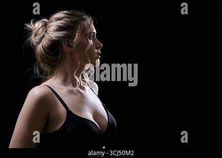 Giovane donna seria su sfondo nero con vista laterale del profilo Foto Stock