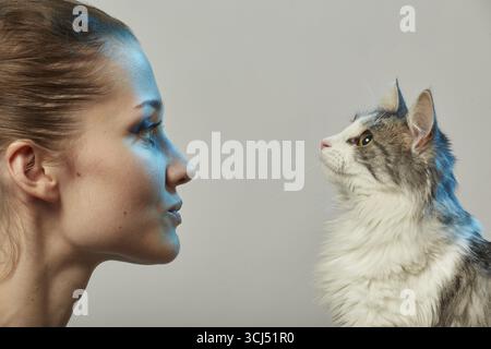 Giovane donna felice con il suo gatto soffice su sfondo nero che lo guarda, sorridente, vista laterale ritratto ravvicinato Foto Stock