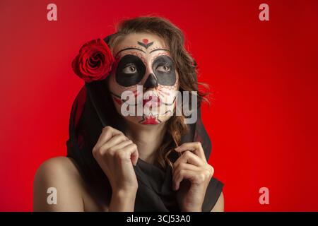 Giovane donna con trucco santa muerte su sfondo rosso Foto Stock