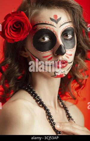 Giovane donna con trucco santa muerte su sfondo rosso Foto Stock