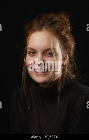 Giovane donna seria e triste con sindrome di Down su sfondo nero che guarda la fotocamera sorridente Foto Stock