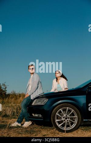 Coppia seduta sul cofano auto in campagna sotto il cielo azzurro Foto Stock