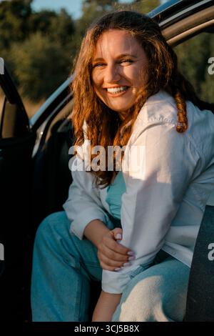 Donna sorridente seduta sulla porta dell'auto Foto Stock