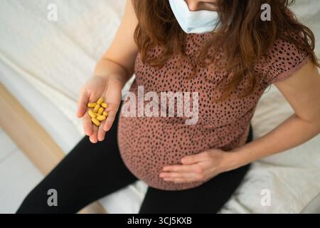 Donna incinta che esamina attentamente la pillola prima dell'assunzione mentre la tocca. Gestione accurata della salute durante il periodo di gestazione. Foto Stock