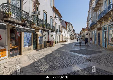 Un'affascinante strada acciottolata a Tomar è costeggiata da edifici storici e piccoli negozi, che invitano i turisti ad esplorare la miscela unica di cultu della città Foto Stock