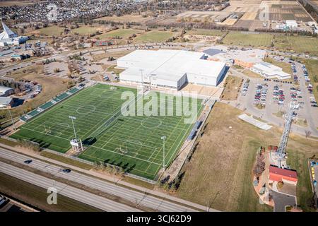 Ampio campo con uno stadio sportivo sullo sfondo. Lo stadio è circondato da una recinzione e dispone di un ampio parcheggio Foto Stock