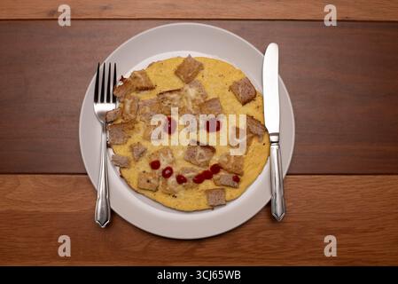 Una deliziosa omelette al formaggio condita con cubetti di pane tostato e un ketchup sorridente. Servito su un piatto bianco con una forchetta e un coltello su un legno Foto Stock
