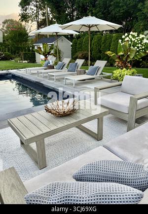 Area lounge con patio e piscina sul retro di lusso e design moderno. Ombrellone, divano, sedie a sdraio, tavolo a bordo piscina. Posti a sedere e solarium con asfaltatrici in pietra grigia. Foto Stock
