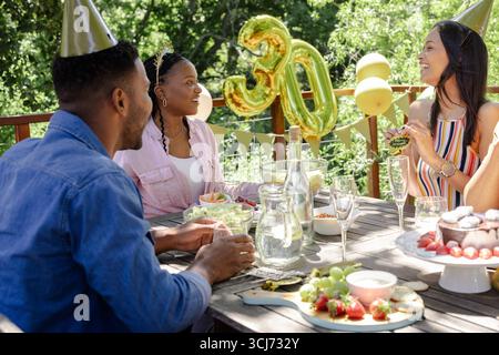 Festeggiando il 30° compleanno, gli amici si divertono a una festa all'aperto con cibo e risate Foto Stock