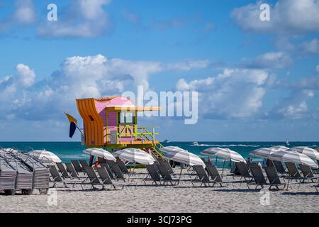 Colorata torre del bagnino con file di sedie da spiaggia bianche e ombrelloni a South Beach, Miami Beach, Florida, Stati Uniti, sotto il cielo blu e le nuvole Foto Stock