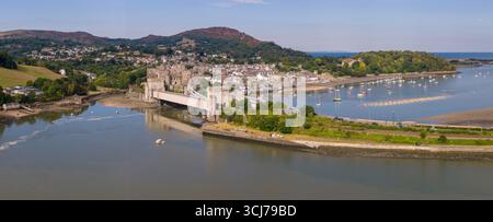 Vista aerea del castello di Conwy, della linea ferroviaria e del ponte stradale che attraversa l'estuario con la città e le montagne sullo sfondo in una soleggiata giornata estiva. Foto Stock