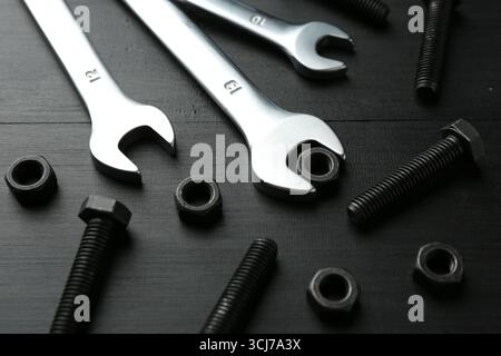 Molte chiavi, bulloni e dadi in metallo su un tavolo di legno nero, primo piano Foto Stock