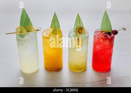 Cocktail tropicali colorati in bicchieri tiki con ghiaccio e frutta esotica su sfondo chiaro Foto Stock