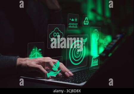 Tecnologia sostenibile e innovazione dell'energia verde. Persona che utilizza un computer portatile con icone verdi che rappresentano energia rinnovabile, riduzione di CO2, riciclaggio, Foto Stock