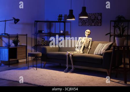 Modello di scheletro umano seduto su un divano nel salotto buio Foto Stock